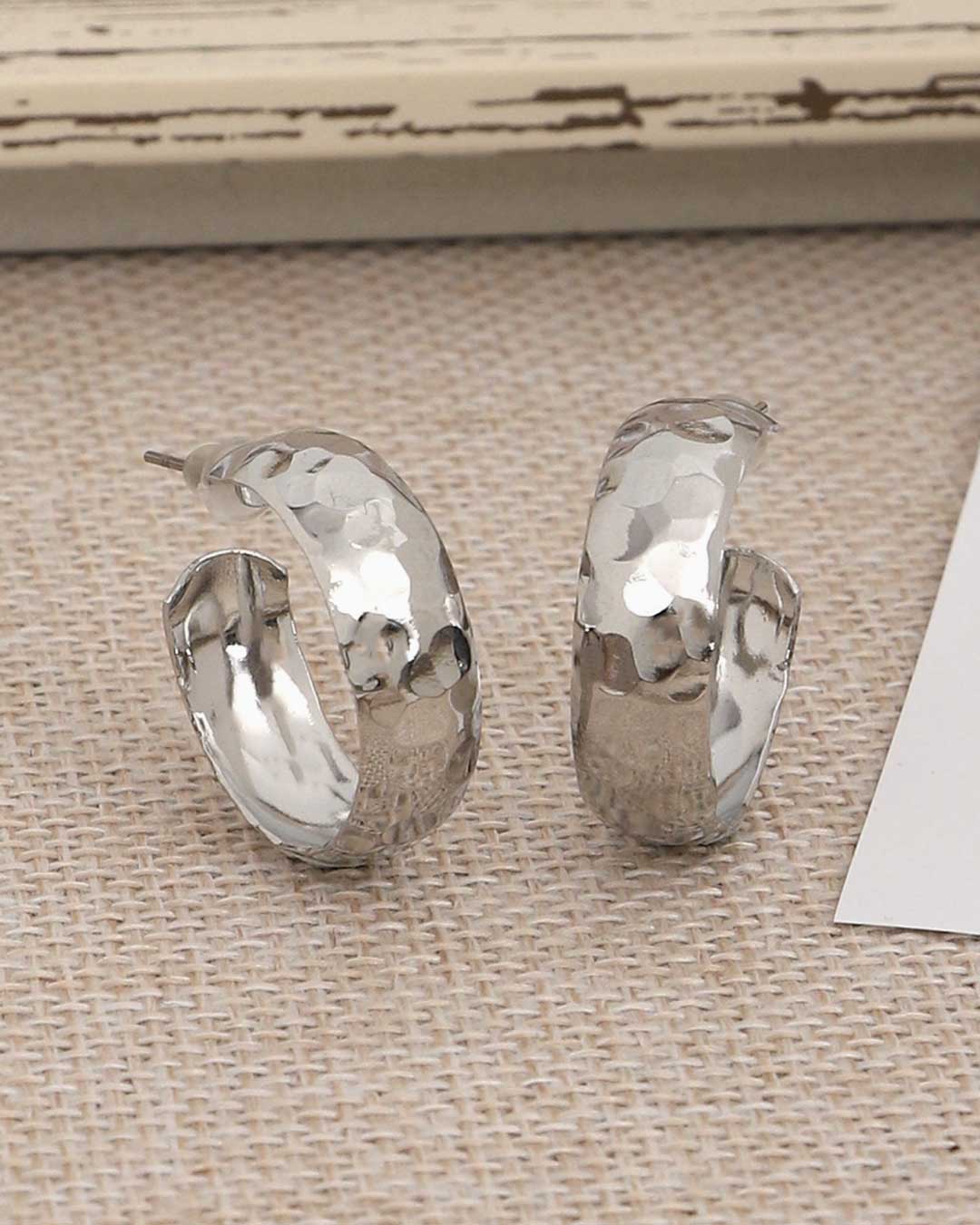 Hand-hammered silver hoop earrings on fabric background
