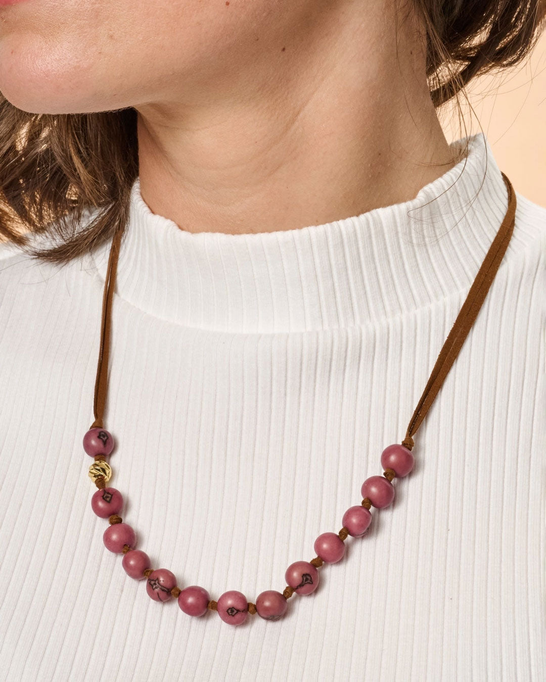 Necklace with pink beads and brown cord worn by a person on a white background