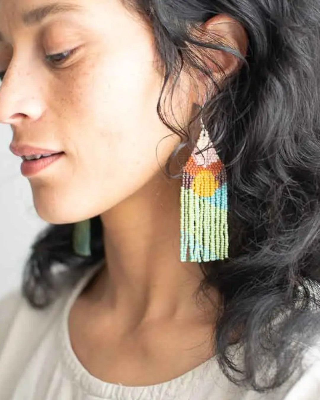 Close-up of a woman wearing colorful beaded earrings with a neutral background