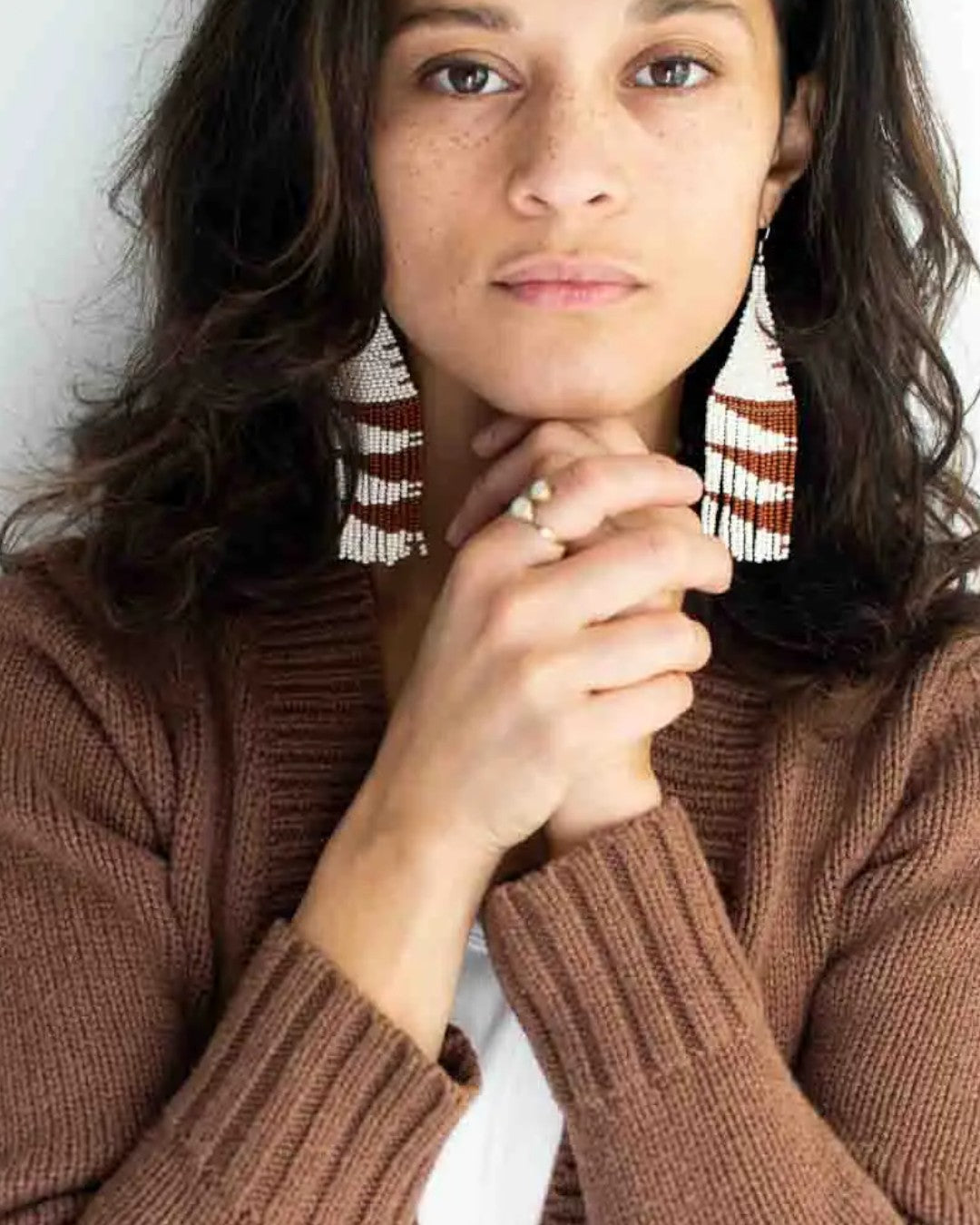 Woman wearing a brown sweater and patterned earrings against a white background