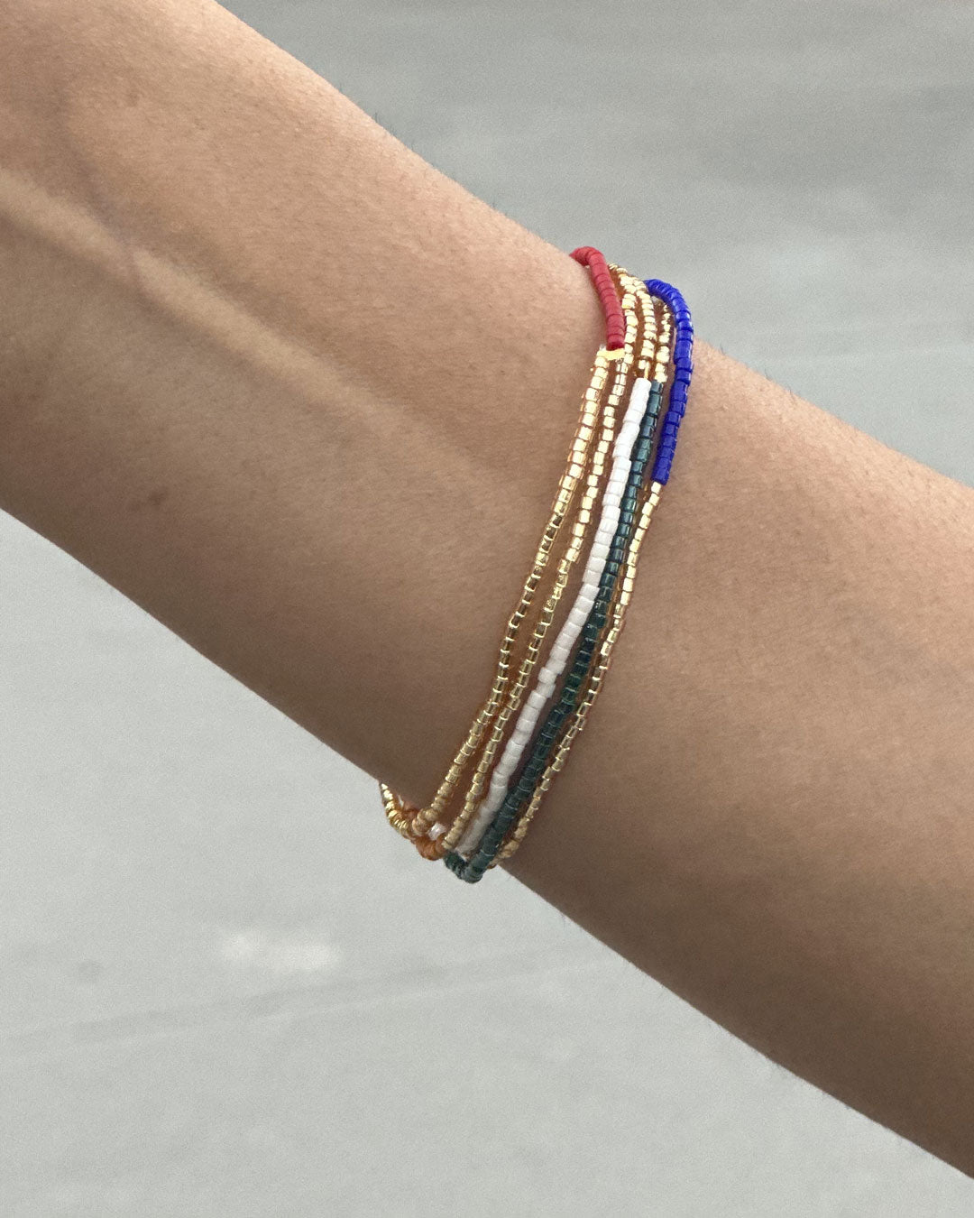 Stack of 5 elastic beaded bracelets in red, blue, green, white, and gold