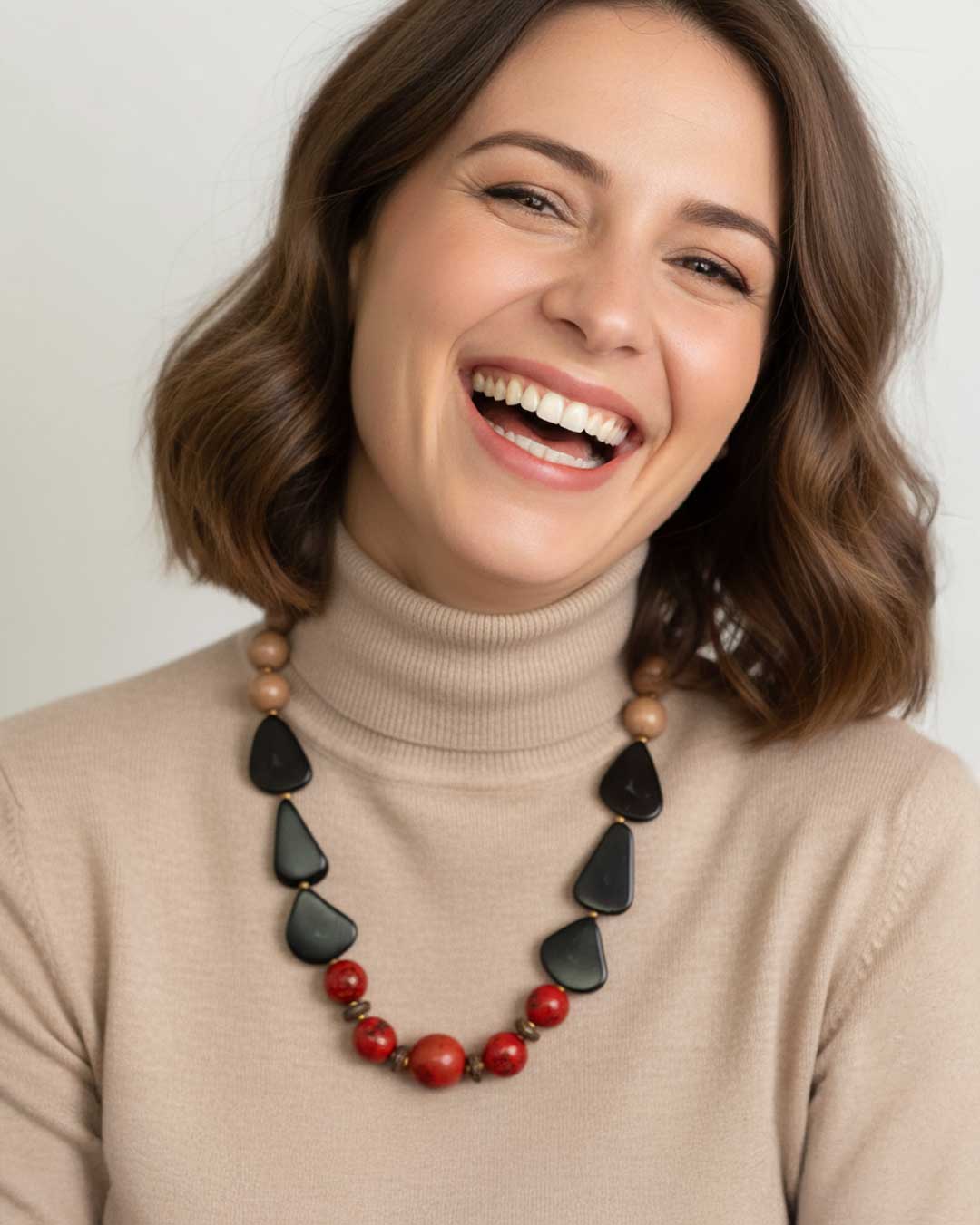 Woman wearing a necklace with black and red beads against a plain background