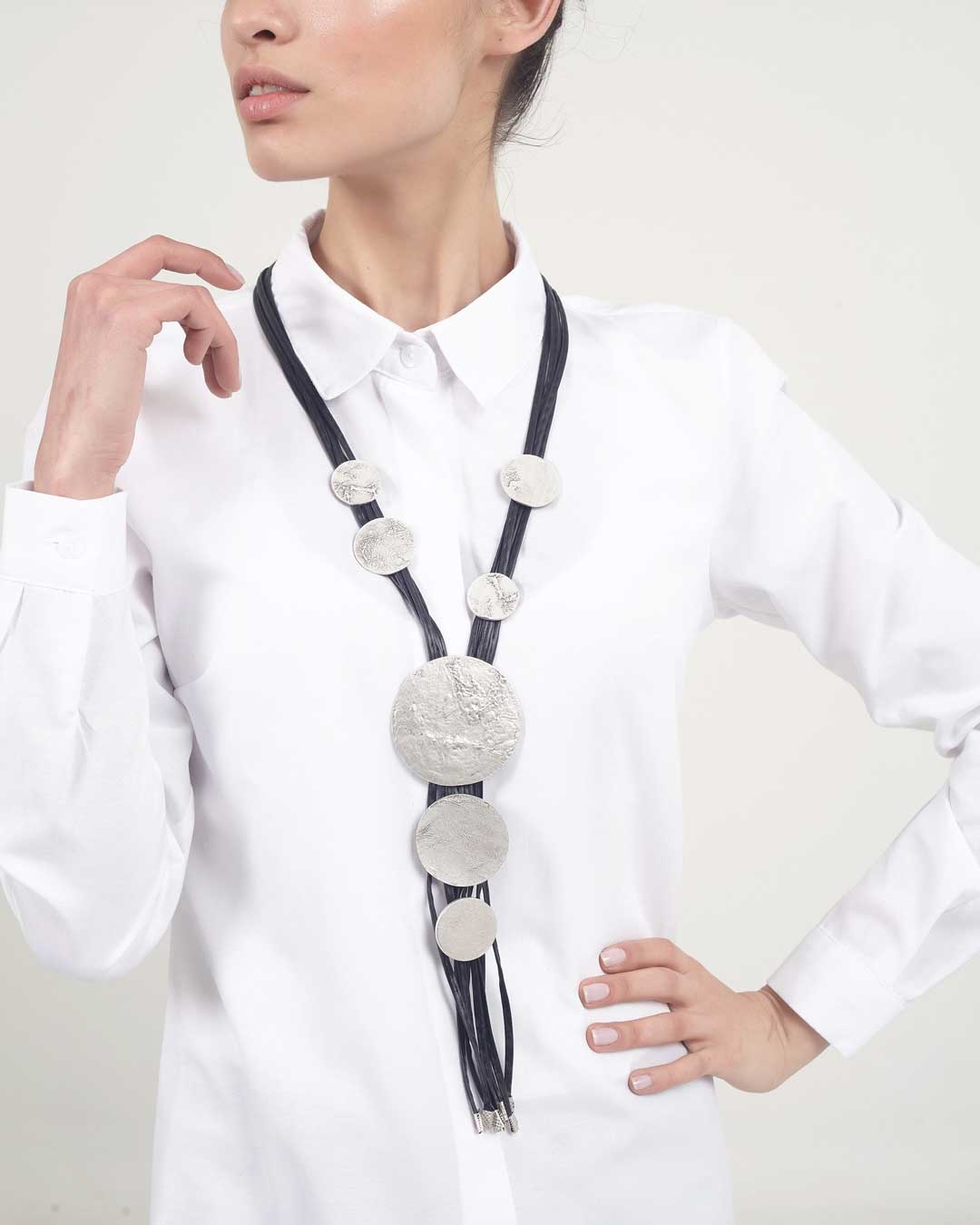 Person wearing a white shirt with a long, decorative necklace.