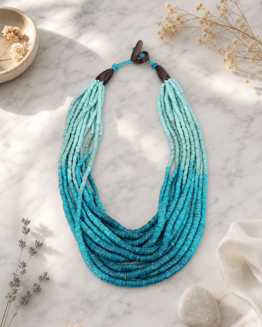 Aqua ombre coconut bead necklace displayed on white marble surface