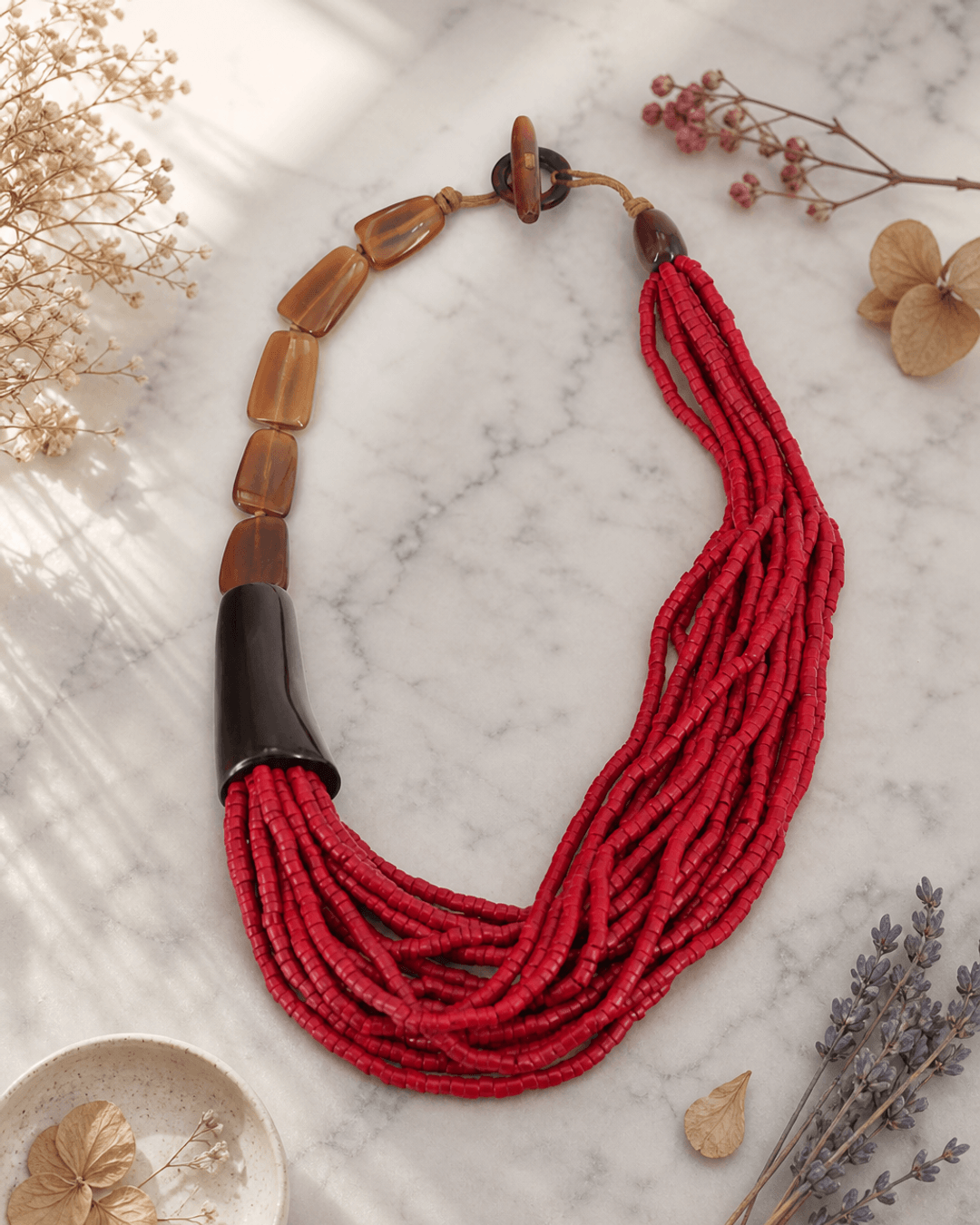 Asymmetric necklace with red horn pendant and natural coconut beads on marble surface