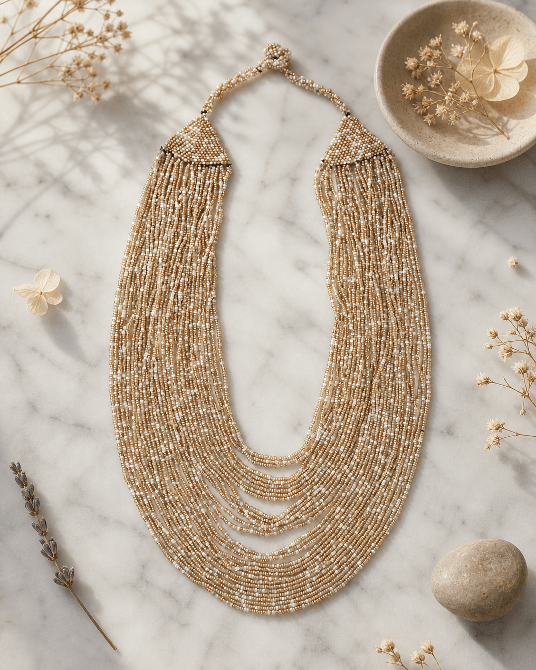 Beige and gold-tone multi-strand glass beaded necklace displayed on white marble surface