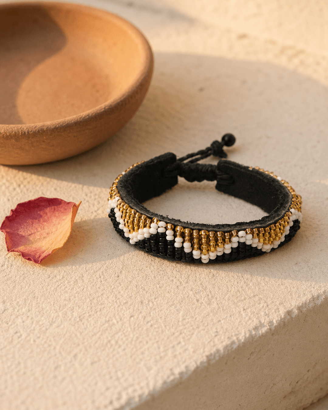 Black and gold beaded Kenyan bracelet displayed on a warm plaster shelf