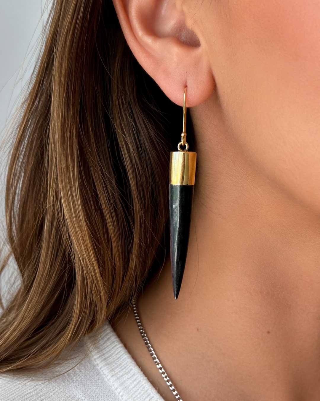 Kami black horn brass spike drop earring worn in ear, close-up profile view showing gold cylindrical cap and long tapered spike