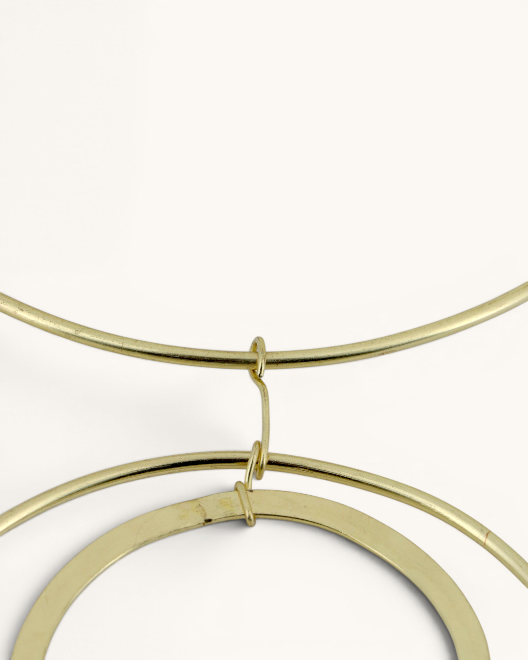 Close-up detail of the brass jump ring connection joining the double ring pendants to the collar necklace