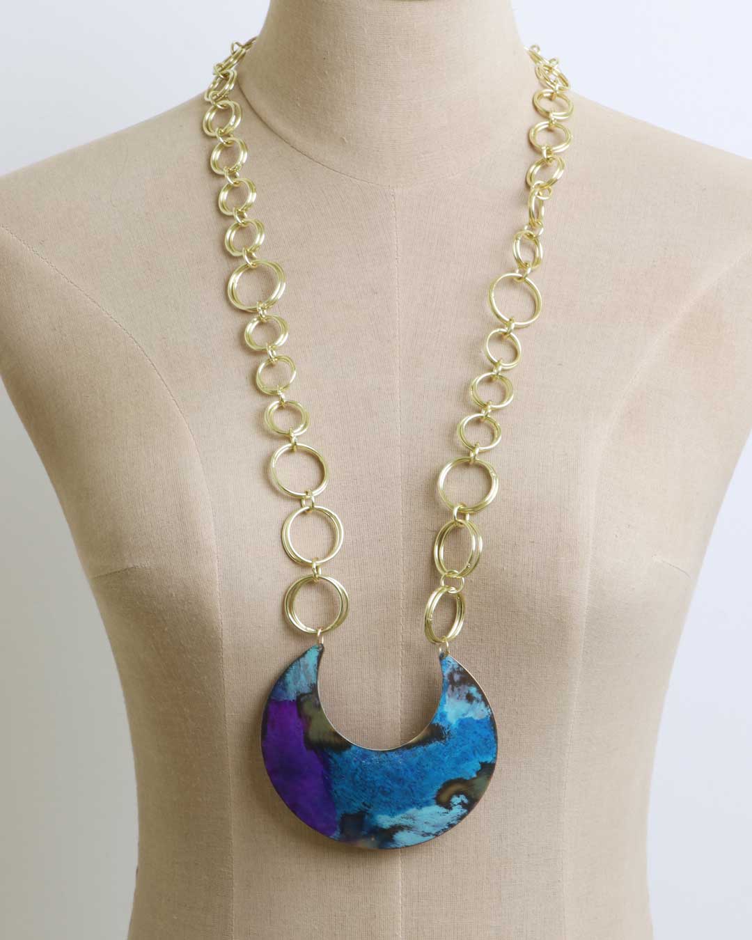Hand-patinated brass crescent pendant necklace on a beige dress form showing pendant length and scale against the body