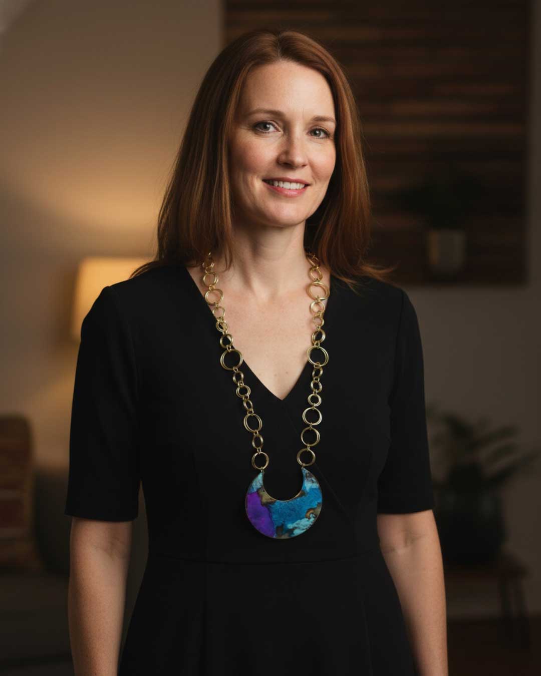 Hand-patinated brass crescent pendant necklace worn by a model in a black dress in a warmly lit indoor setting