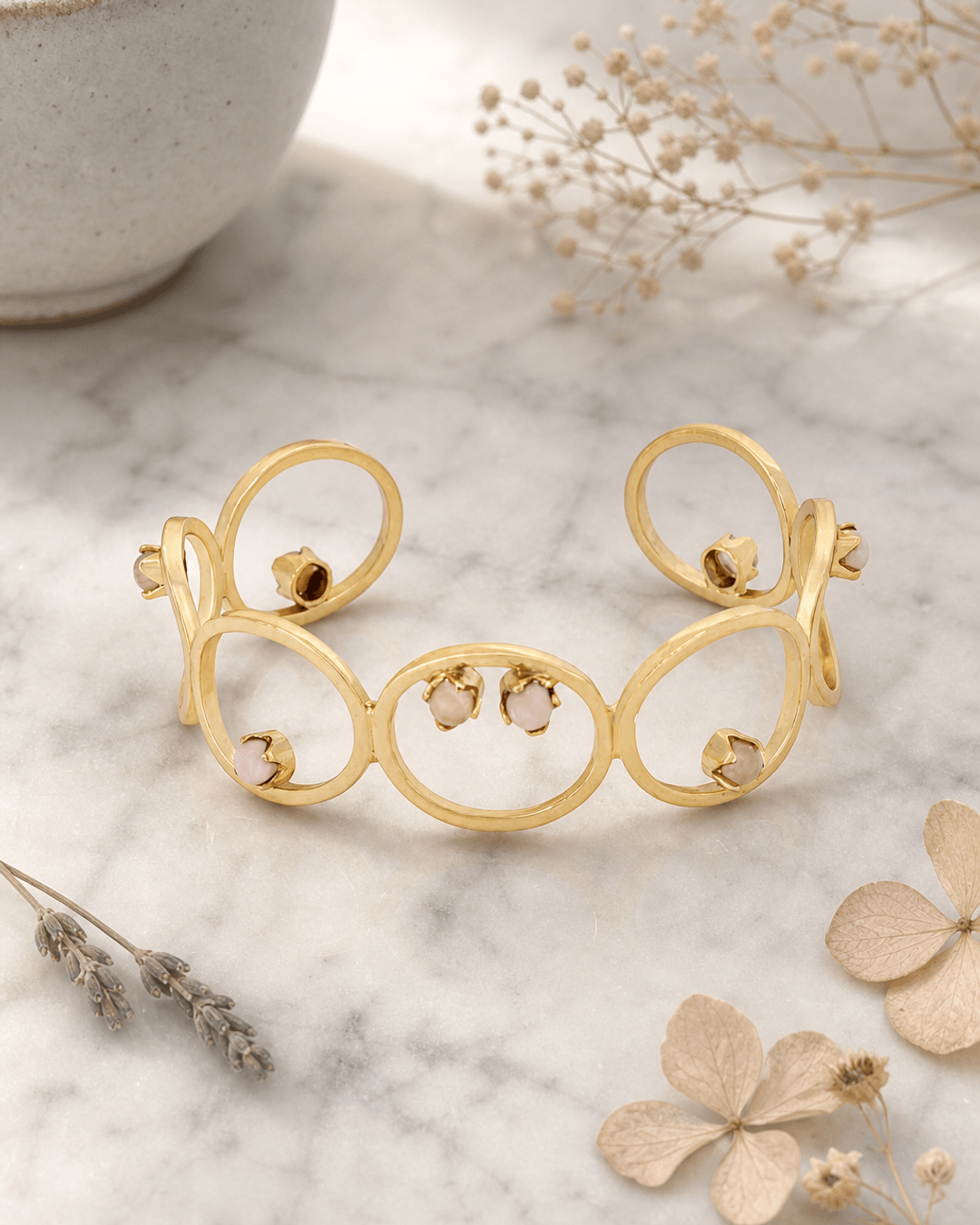 Brass cuff bracelet with opal and rose quartz stones on marble surface