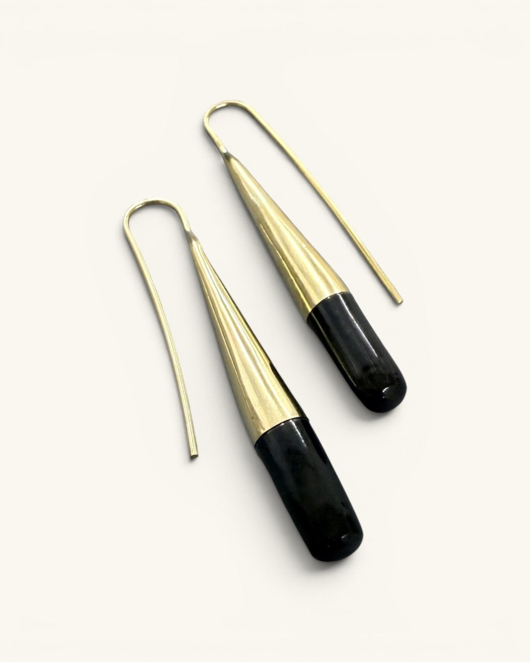 Tosha brass horn threader earrings angled flat on white background, close view of brass fluting and black horn drop texture