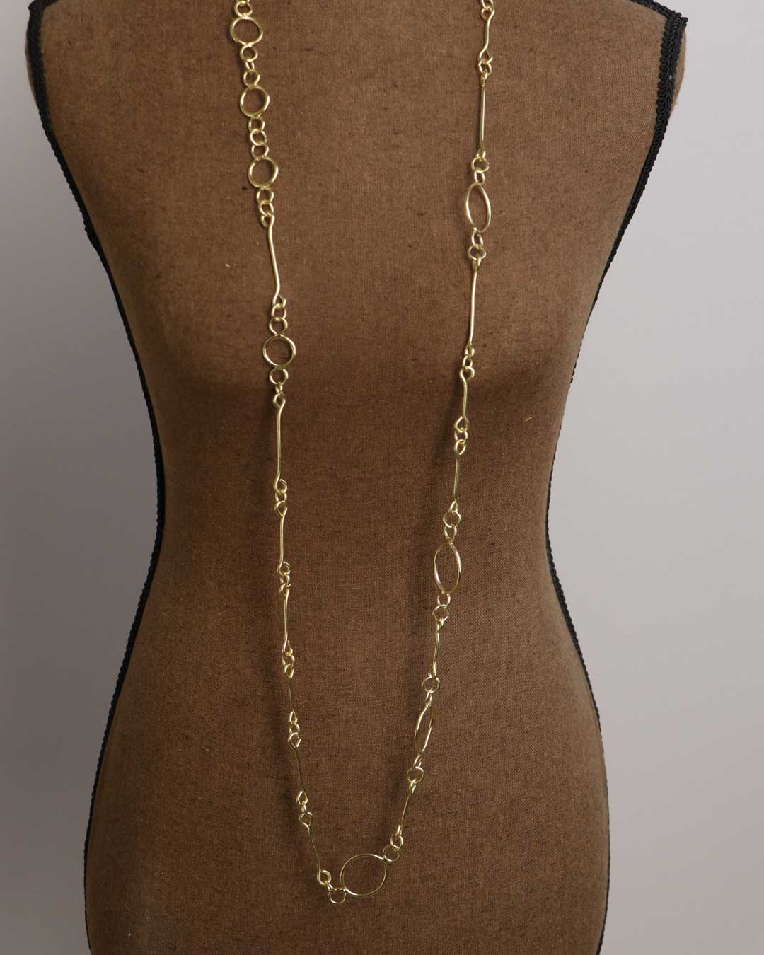 Brass link geometry long wrap necklace as single unlooped strand on dress form, showing full drop length to waist