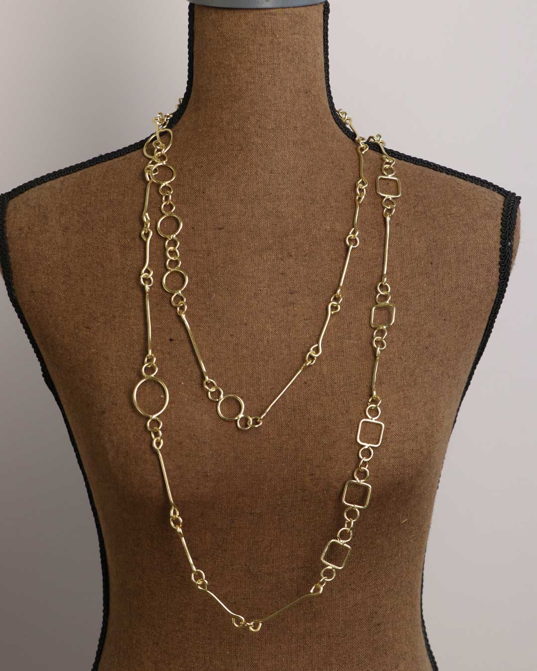 Brass link geometry long wrap necklace as single strand on dress form, front view showing full torso length