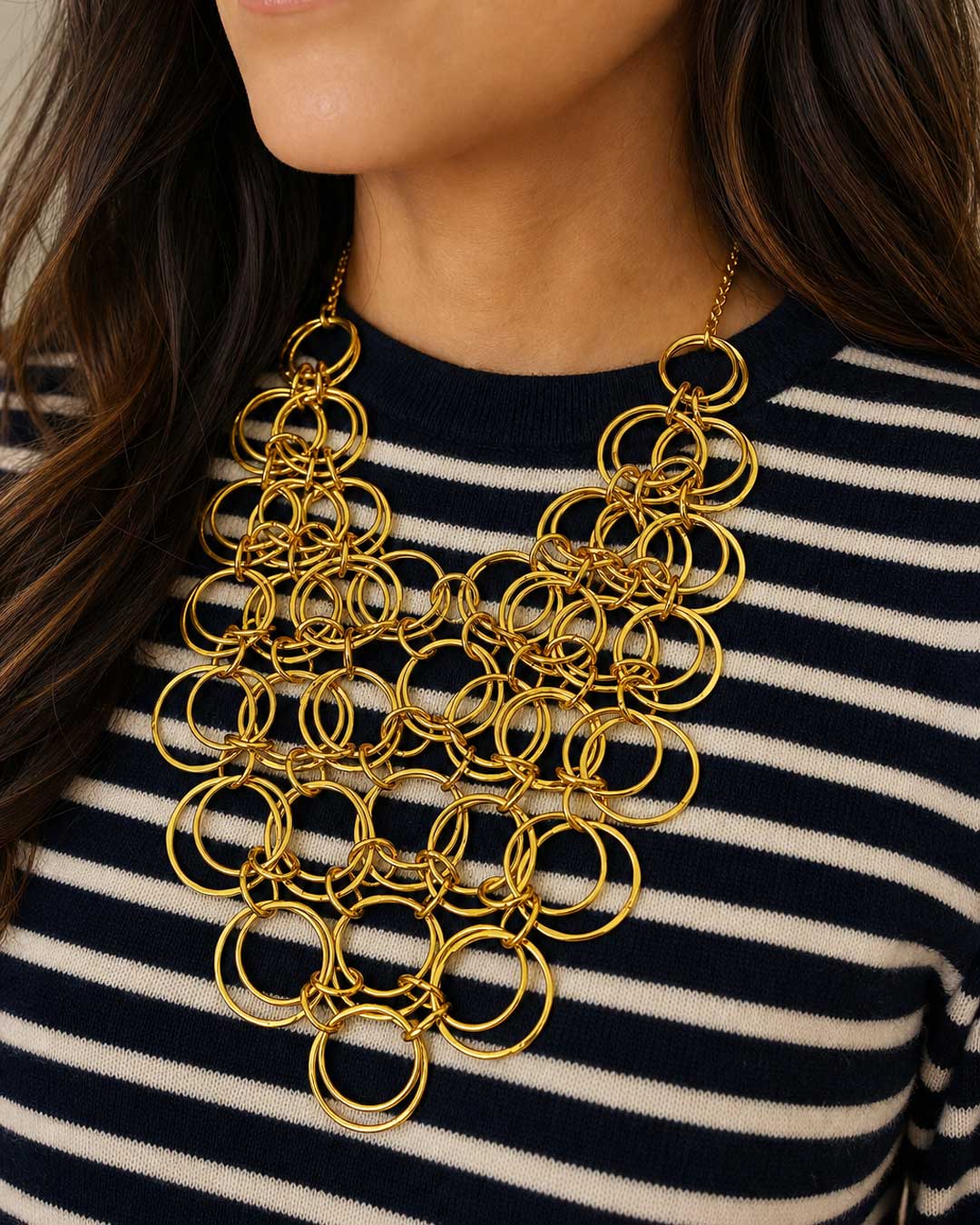 Brass ring bib necklace worn by a model over a navy and white striped sweater, showing full drape on the chest