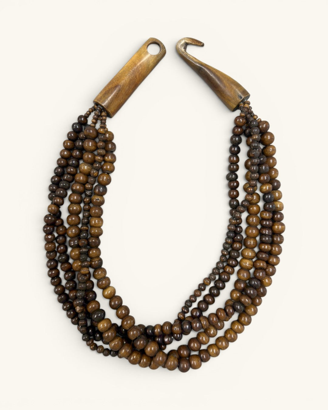 Brown five-strand beaded necklace with wooden toggle clasp unhooked and open, flat lay on cream background