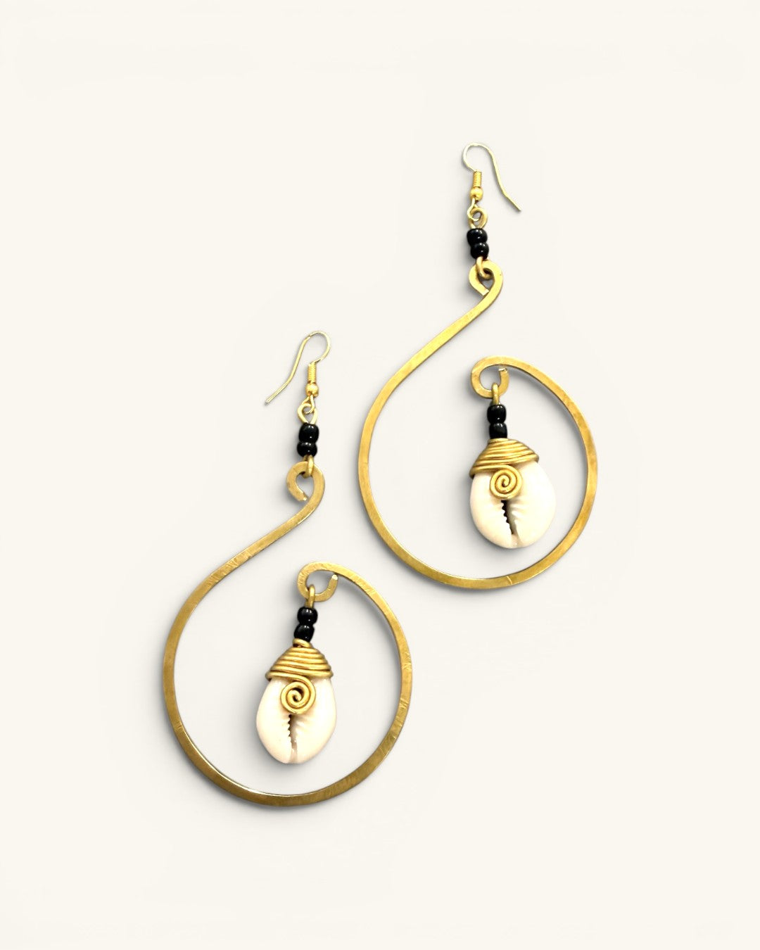Mombasa cowrie shell and hammered brass hoop earrings, both pieces on white background with brass wire-wrapped shells and black beads
