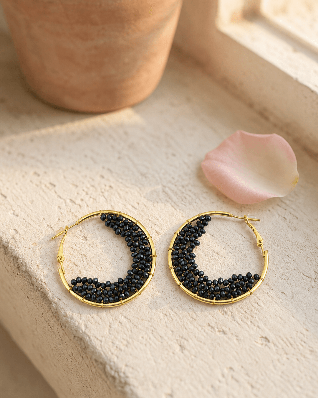 Black beaded crescent hoop earrings resting on a sunlit outdoor window ledge