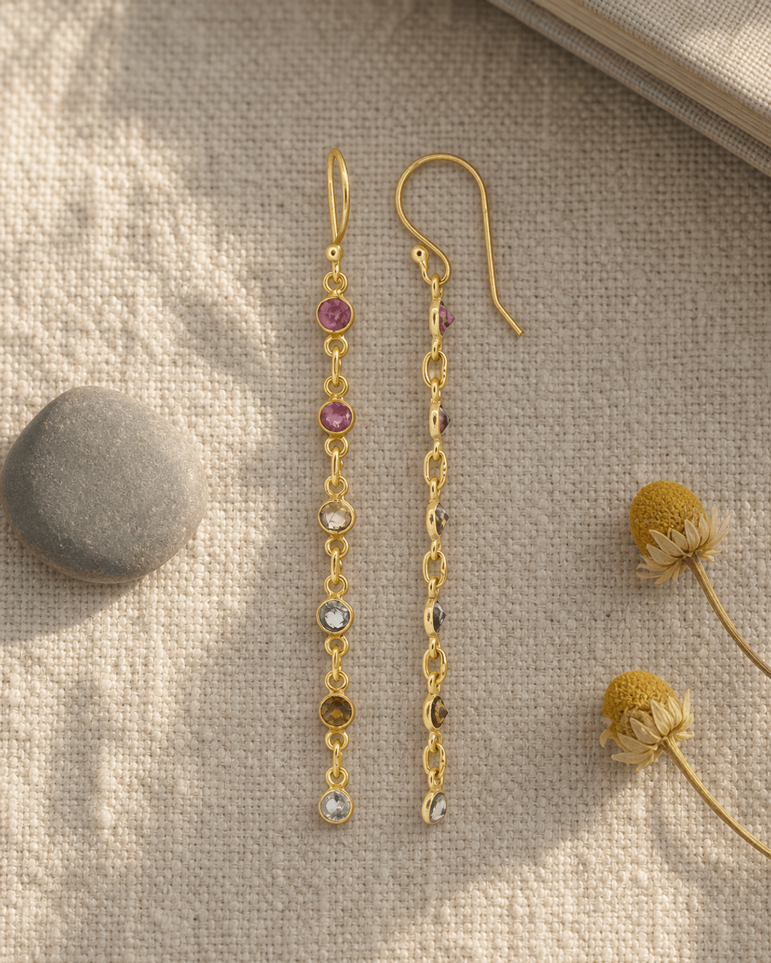 Dainty multi-color tourmaline dangle earrings displayed on a linen journal flatlay
