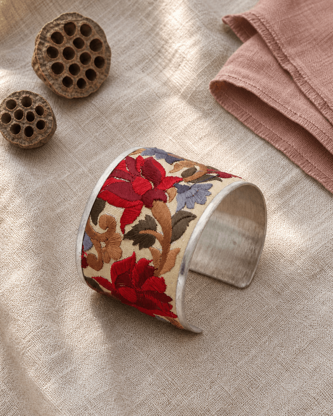Embroidered lotus cuff bracelet in gold thread on linen fabric beside an open journal
