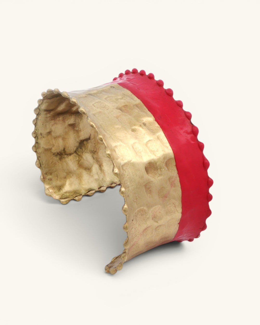 Hand-hammered brass cuff bracelet angled side view showing red painted band stripe and scalloped edges on white background