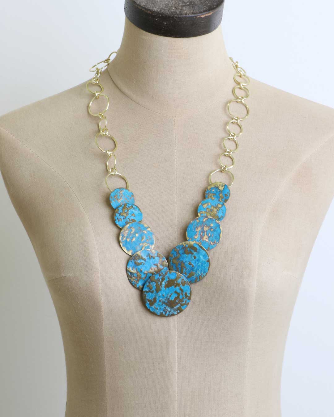 Hand-forged brass statement necklace with blue patina discs, primary front view displaying the complete necklace design