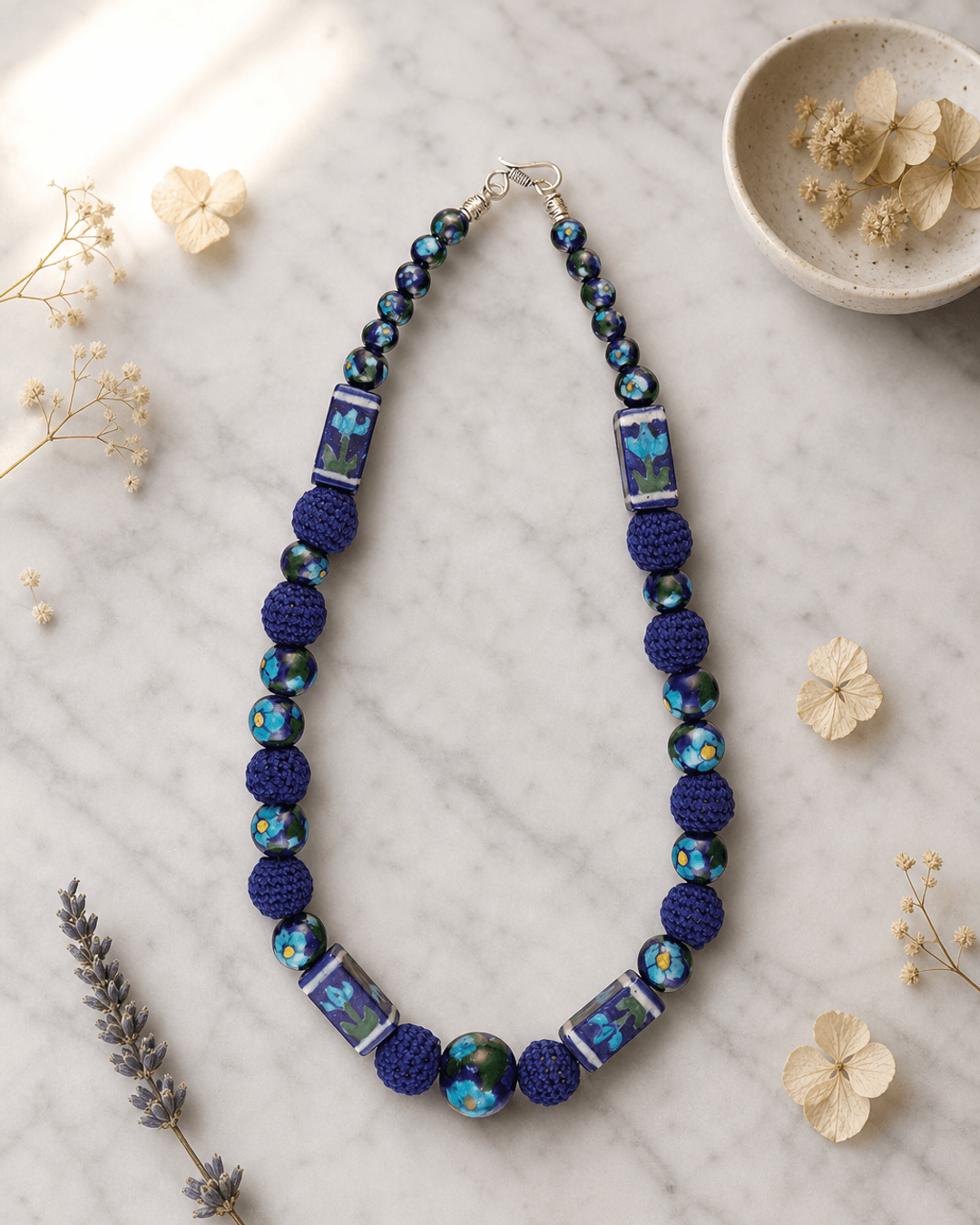 Hand-Painted Floral Ceramic Bead Necklace with Crochet Accents — necklaces, editorial marble lifestyle photo
