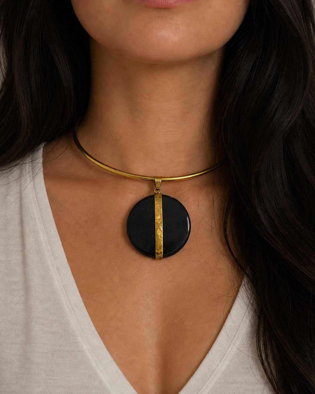 Horn and brass disc choker necklace worn by model, close-up showing black horn disc pendant with brass bar on gold collar