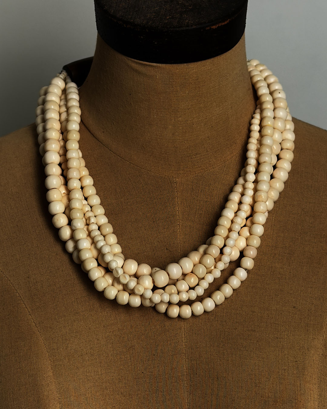 Indian bone bead 5-strand layered necklace draped on a tan dress form, front view showing bead arrangement and drape