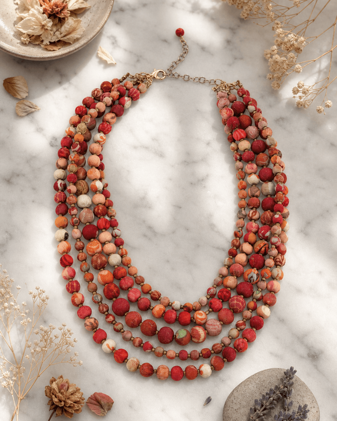 Kantha five-strand layered necklace with colorful embroidered fabric beads displayed on white marble surface