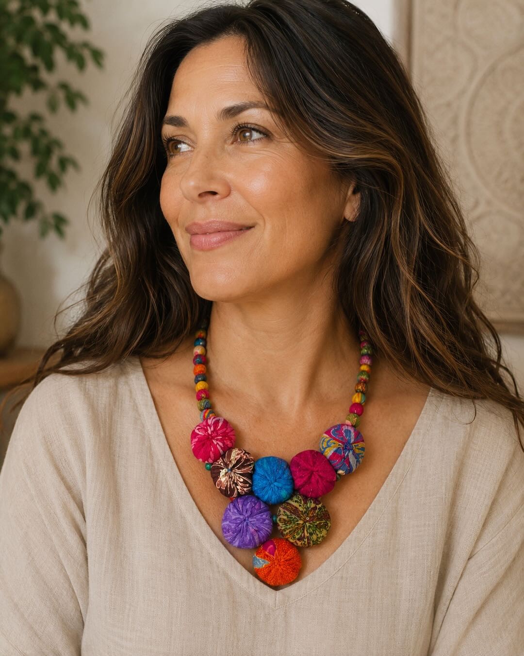 Kantha recycled textile layered bead necklace worn by a woman in a beige linen top, showing colorful fabric medallion pendant at neckline