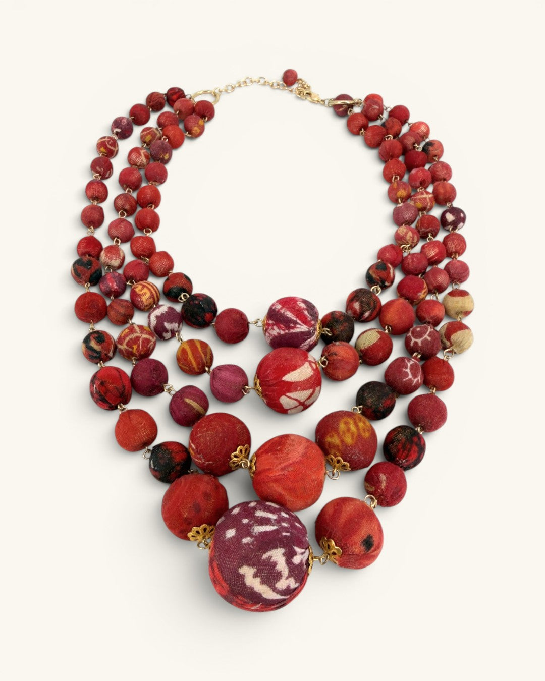 Kantha sari four-strand statement necklace in red tones, angled flat lay highlighting graduated bead sizes toward center drop