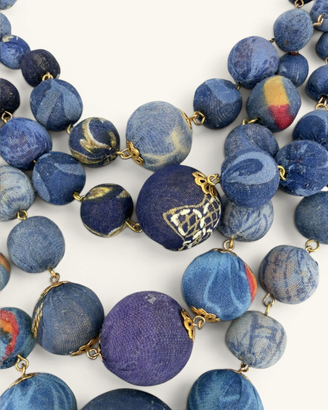 Close-up detail of blue kantha sari fabric beads with printed and marbled patterns, connected by gold wire and findings