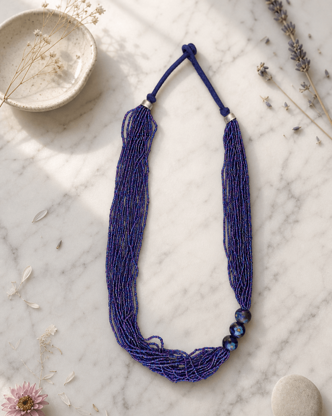 Multi-Strand Blue Glass Bead Necklace with Hand-Painted Ceramic Accents — necklaces, editorial marble lifestyle photo