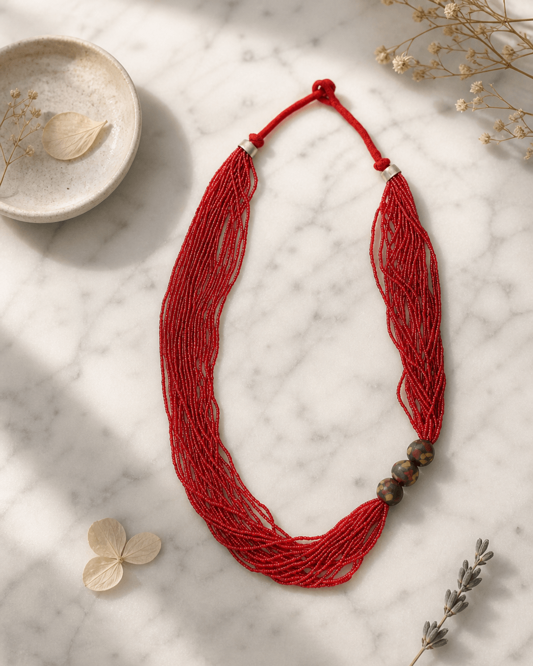 Multi-Strand Red Glass Bead Necklace with Hand-Painted Ceramic Accents — necklaces, editorial marble lifestyle photo