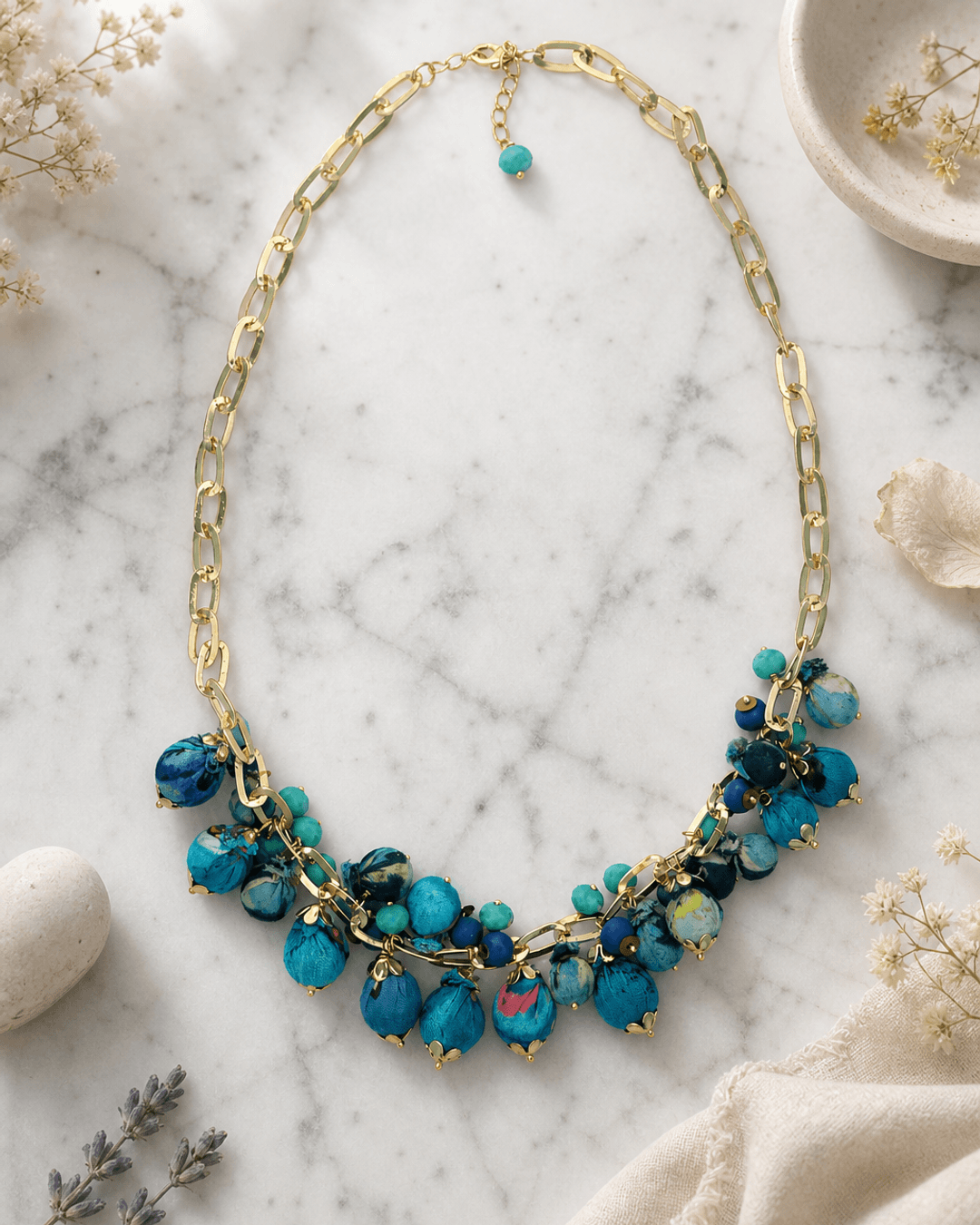 Blue beaded necklace with textile accents displayed on white marble surface