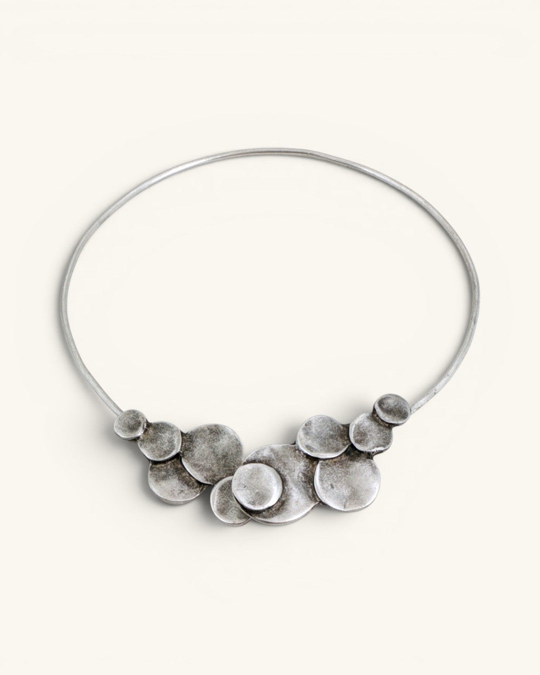 Silver-plated pewter collar necklace with stacked disc cluster centered at front, shown on off-white background