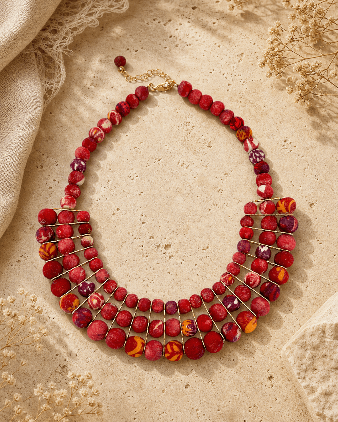 Red textile-wrapped bead layered bib necklace displayed on travertine surface