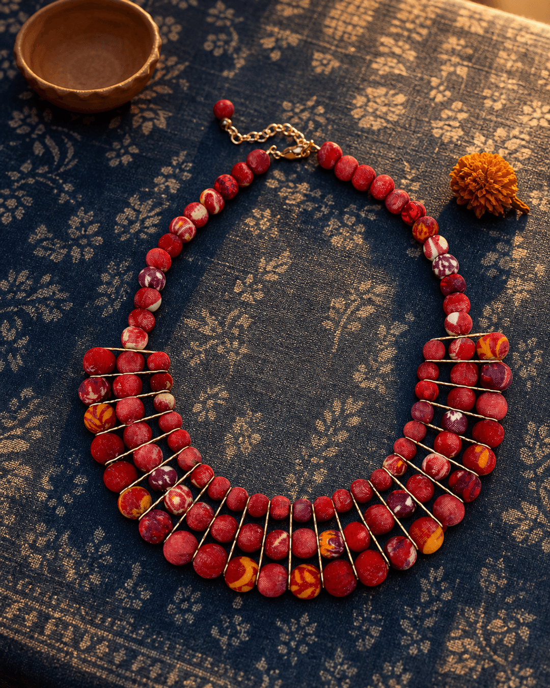 Red textile-wrapped beaded layered bib necklace on indigo fabric background with rim lighting