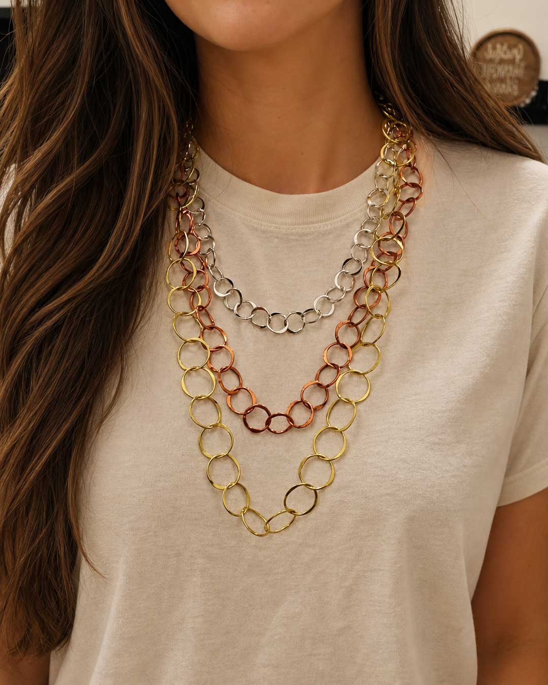 Three-strand mixed metal chain necklace worn close-up on a model's chest, with gold, copper, and silver circular link strands layered