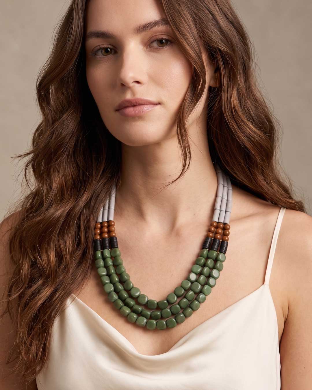 Triple strand magnesite, serpentine and vulcanite beaded necklace worn by a model over a white satin top, front view