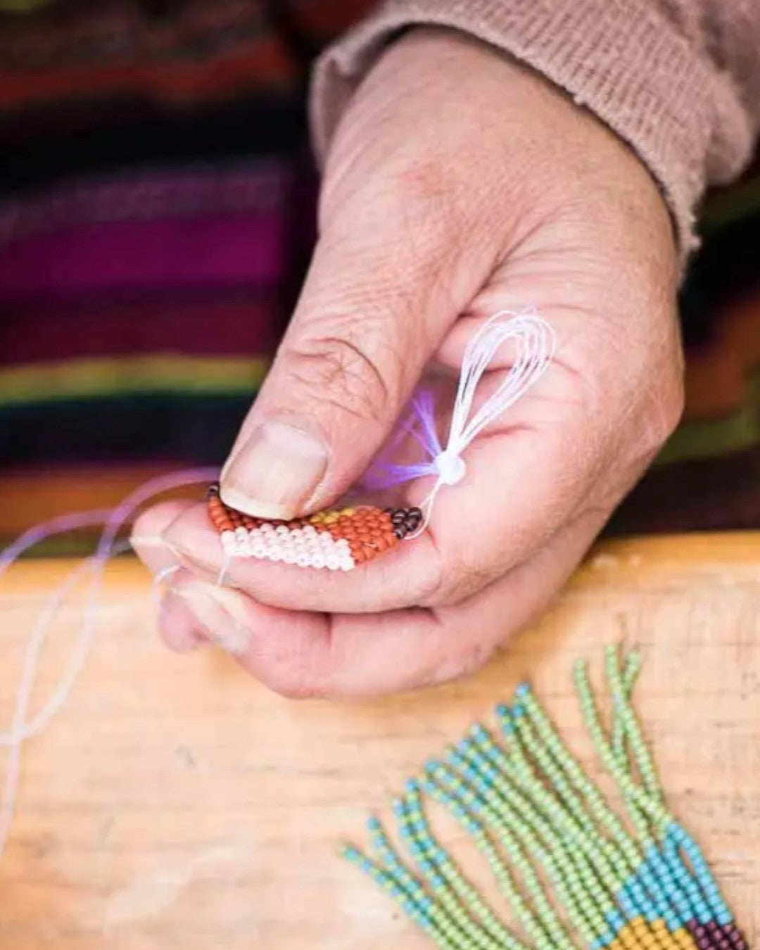 Hand holding a small beaded item with a colorful background