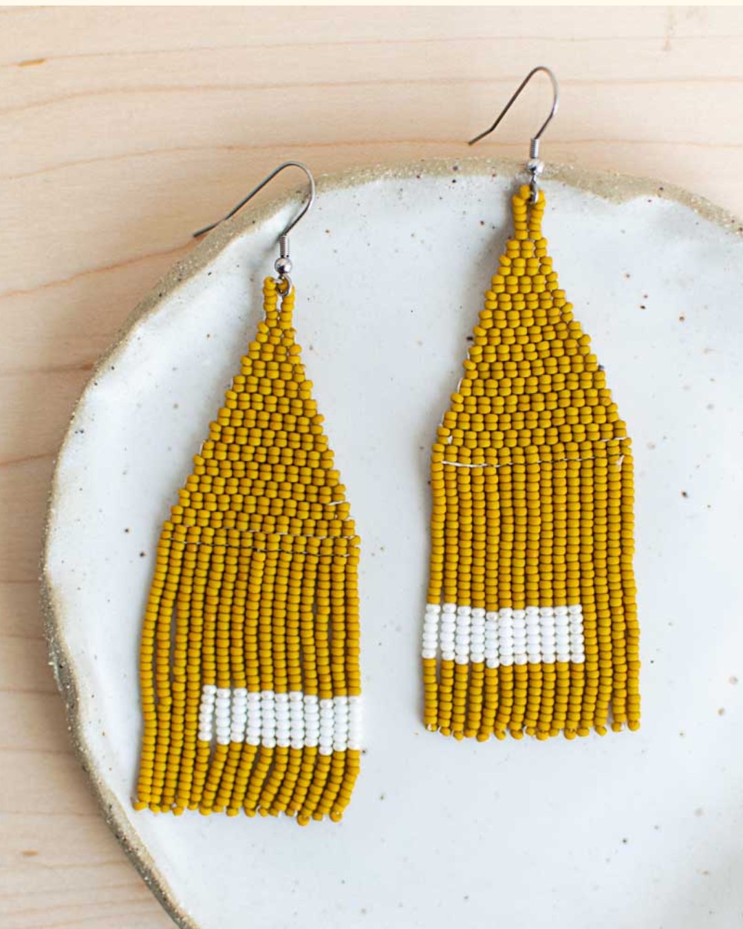 Mustard yellow beaded earrings with white stripes on a ceramic plate.