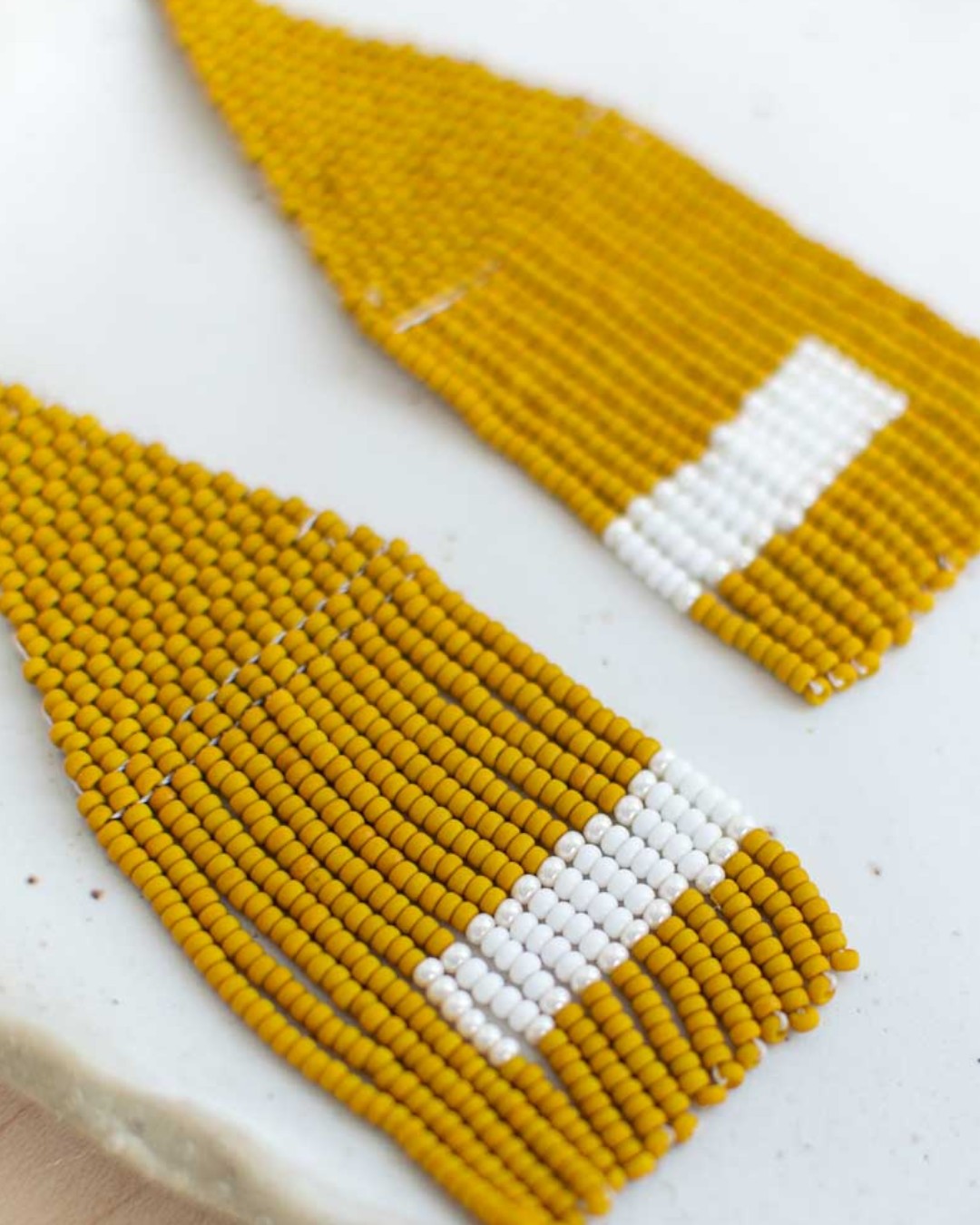 Two yellow beaded earrings with white accents on a white background