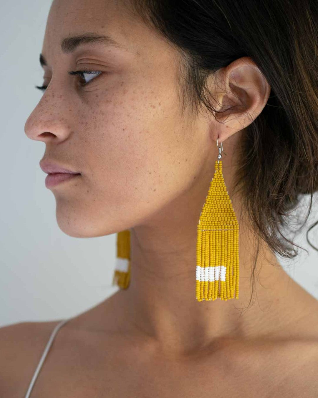 Close-up of a woman wearing yellow beaded tassel earrings against a white background