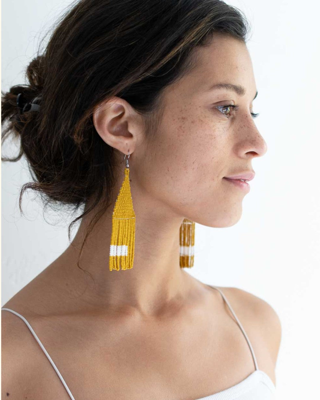 Woman wearing yellow tassel earrings on a white background