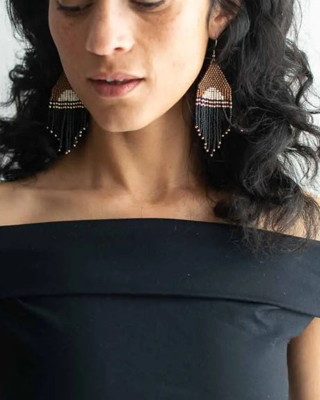 Woman wearing black off-shoulder top and beaded earrings with a neutral background