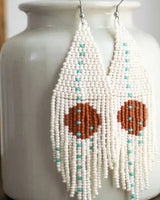 Beaded earrings with heart-shaped brown centers on a white vase.