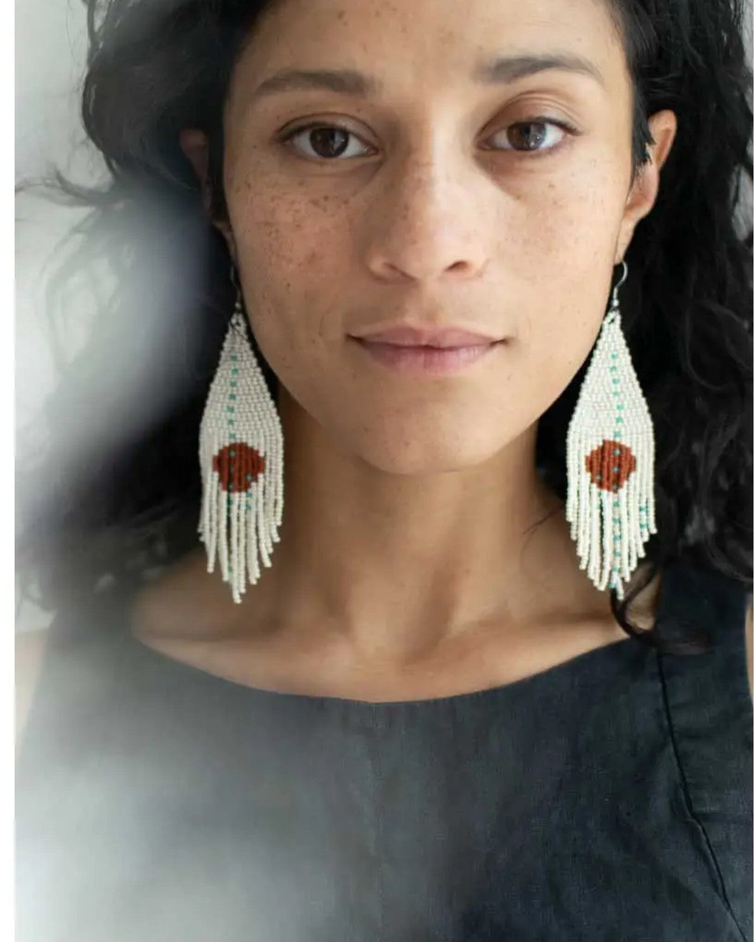 Woman wearing long, beaded earrings with a neutral background